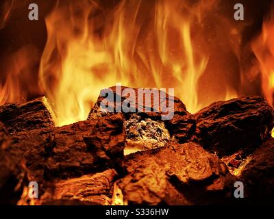 Close-up view of hot coals on a lit fire in the home. Fireplace with a warm orange glow and flames. Copy space to top Stock Photo