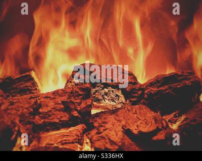 A close up selective focus shot inside a fireplace. Details of hot coals with orange and yellow rising flames. Atmospheric lighting with copy space Stock Photo