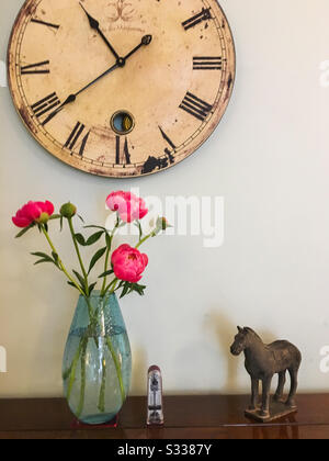 A still life photograph featuring peony flowers, a clock, a metronome and an oriental horse ornament. Stock Photo