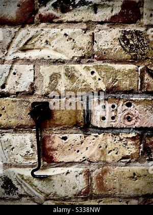 Brick wall worn down by metal door latch which is hanging down. Other marks and holes eroded and warn into h texture. Stock Photo