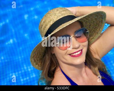Portrait of woman wearing blue bikini, sunglasses and straw hat, near the pool Stock Photo