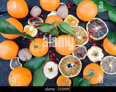 Flat lay of tangerines with red berries and dry fruits like apple slices, orange slices placed on rustic wooden table Stock Photo