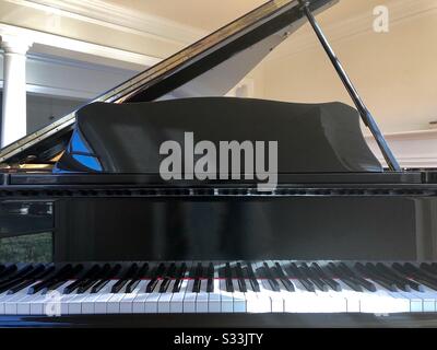 View of the keyboard, open top, music stand, keyboard cover, and keys of a baby grand piano. View is as if sitting on the bench in front of the piano, and sunlight is falling on part of the keyboard. Stock Photo