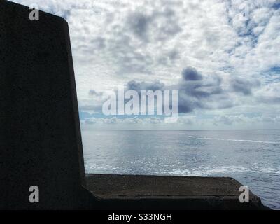 The flat shimmering peaceful ocean reflecting the cloudy sky above , view from the breakwall, Coffs Harbour Australia Stock Photo