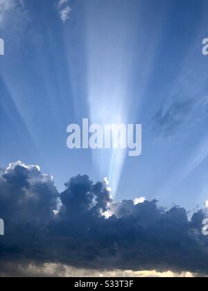 A ray of sunlight bursts through some dark clouds looming at sunset Stock Photo