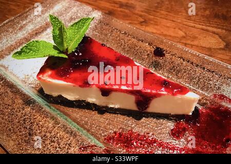 Slice of cheesecake with cranberry jam on glass plate, decorated with mint leaf. Stock Photo