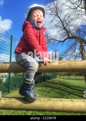 Three year old boy stuck climbing over a fence. Stock Photo