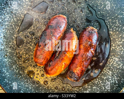 3 sausages frying in a pan Stock Photo