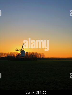 Silhouette of windmill on hill with sun setting behind. Stock Photo