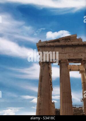 The ruins of the Erechtheion Temple on the Acropolis in Athens stands tall in front of a blue sky full of wispy clouds.