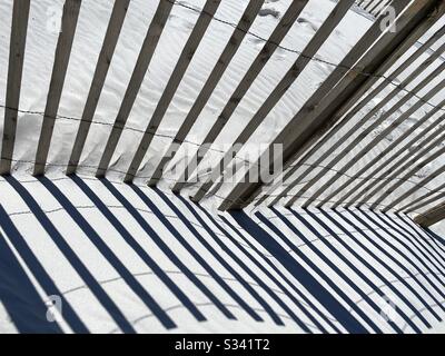 Abstract of lines and patterns of a wooden fence onto white sand on the beach Stock Photo