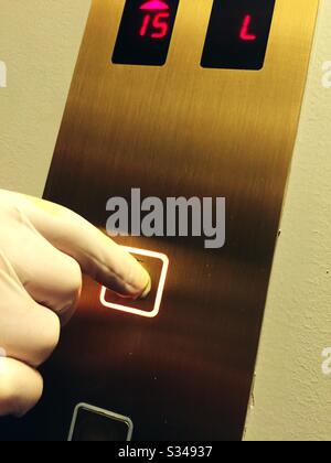 Man pressing an elevator button wearing latex gloves in order to prevent the spread of the coronavirus during the global pandemic of COVID-19, USA Stock Photo