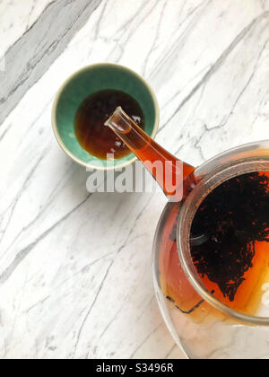 Pu-erh loose leaf tea from China poured from a glass tea pot into a glazed green ceramic cup. This type of fermented black tea is healthful and aids in digestion of fats. Stock Photo