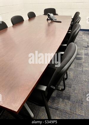 Angle view of a conference room with wood conference table and 10 black chairs with a phone on the table Stock Photo