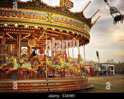 A view of a Victorian style galloping carousel at a travelling fairground. Horse merry go round with gold and orange colours at an amusement park during sunset