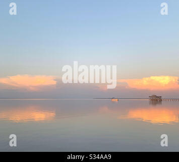 Colorful sunset skies over bay water with boat dock and reflections on ...