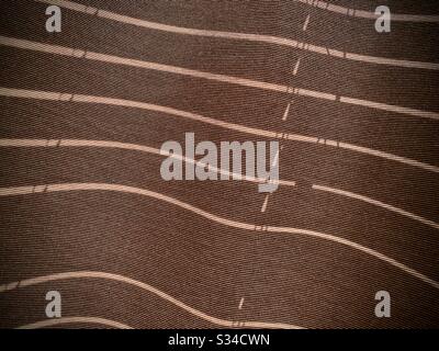 Abstract pattern of sunlight and shadow from window blinds on rough textured curtain, creating earth-tone color background Stock Photo