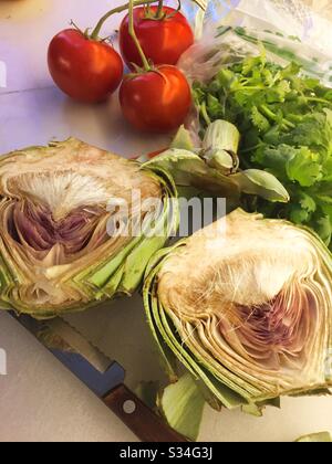 Close up of a sliced artichoke, tomatoes and cilantro bunch on a residential kitchen cutting board, USA Stock Photo