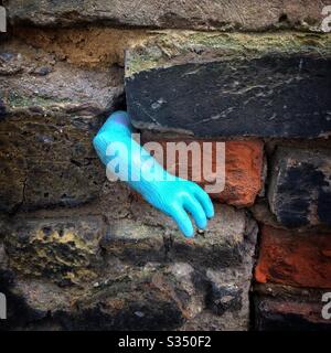 Cabin fever. The arm of a blue plastic toy emerges from some brickwork, looking as if the creature is trying to escape from inside Stock Photo