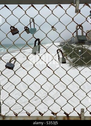 Rusty padlocks on a chain link fence with view of the beach in the background Stock Photo