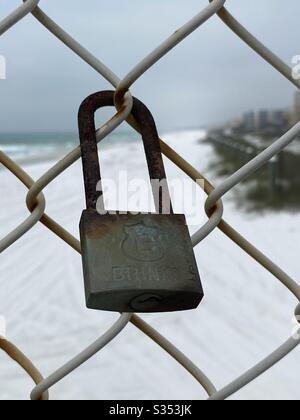 Closeup of a rusted padlock on a chain link fence with white sand beach background Stock Photo