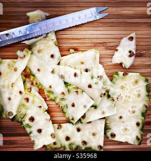 Preparing a whole pineapple in the kitchen. Fresh and ripe fruit preparation. Ingredients for homemade pineapple salsa. Peeled skin on a wooden chopping board with knife Stock Photo