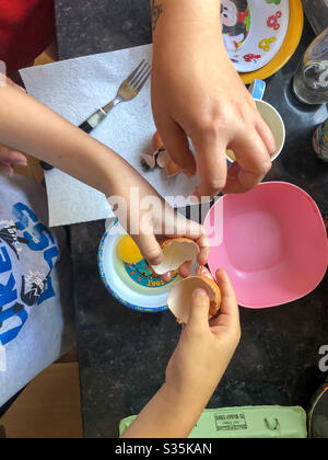 Mother and son cracking an egg into a plastic bowl, seen from above. Stock Photo