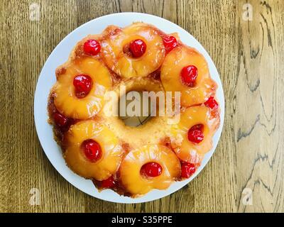 A pineapple upside down cake on a white plate at a wooden table. Stock Photo