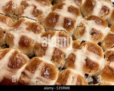 Overhead view, detail of freshly baked, fruit-filled Hot Cross Buns, cooling on a rack. Traditional Good Friday / Easter baked goods. Stock Photo