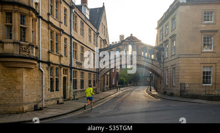 A lone jogger in early morning sunlight in Oxford: New College Lane, under the Bridge of Sighs (Hertford College). During the coronavirus / Covid-19 lockdown the streets are empty. Stock Photo