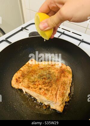 Squeezing lemon over salmon frying in a pan Stock Photo