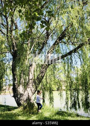 Little girl playing under a willow tree Stock Photo