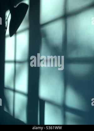 Sunlight and shadows forming multiple shapes and patterns on a blue green teal coloured wall Stock Photo
