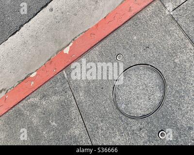 Manhole cover in sidewalk next to red curb, creating a grungy abstract background for text and graphics Stock Photo