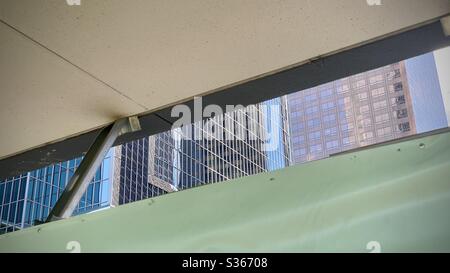 LOS ANGELES, CA, APR 2020: windows of tall office blocks reflecting the sky, glimpsed through a gap between ceiling and green tarpaulin in Downtown Stock Photo