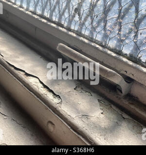 Detail of old, cracked, dirty white paint on a window frame with handle, and daylight coming through wire-mesh safety glass Stock Photo