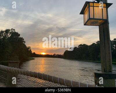 Lake with the sunset in the distance taken from a bridge with a lantern above Stock Photo