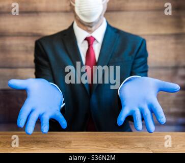 A businessman, doctor or employer sitting at a desk wearing ppe blue surgical gloves and face mask Stock Photo