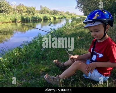 4 years old boy child sitting on lake shore holding a twig as fishing rod in summer, Ferto-to, Fertorakos, Hungary Stock Photo