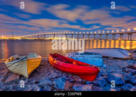 Colorful dinghy boats in the foreground with the Coronado Bay bridge in the distance under a cloudy twilight sky Stock Photo