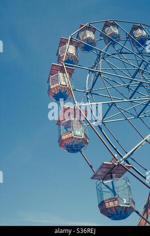 A close up low angle view of the suspended seats of a Ferris Wheel at a fairground under a clear blue sky Stock Photo