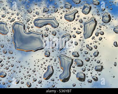 Droplets of rain on a glass table top with the sky and clouds reflected on the surface Stock Photo