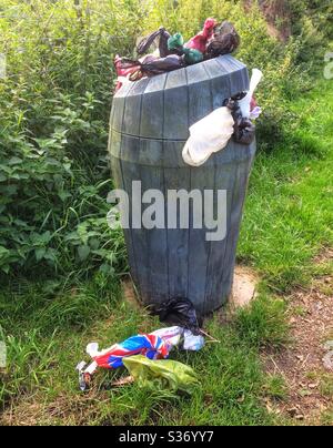 Overflowing park waste bin with dog poo bags on the floor. Stock Photo