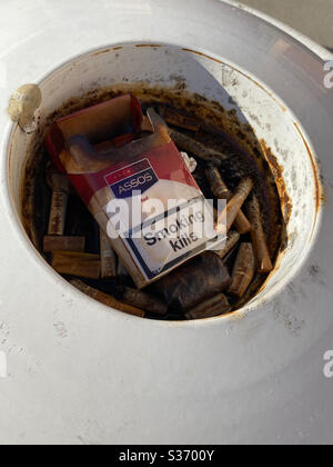 Dirty outdoor cigarette ashtray with a pack of empty cigarettes that says smoking kills Stock Photo
