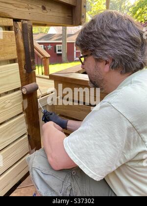 One man staining deck boards with roller Stock Photo