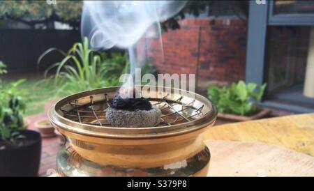 Burning resin outdoors on top of a bamboo charcoal disc using a brass incense burner. Stock Photo