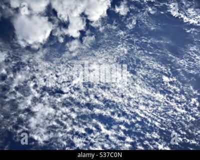 Abstract summer sky scene. White fluffy clouds are seen against a summery blue background during midday sunshine. Summertime skyscape with copy space. Stock Photo