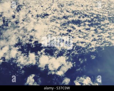 Abstract summer sky scene. White fluffy clouds are seen against a summery blue background during midday sunshine. Summertime skyscape with copy space. Stock Photo
