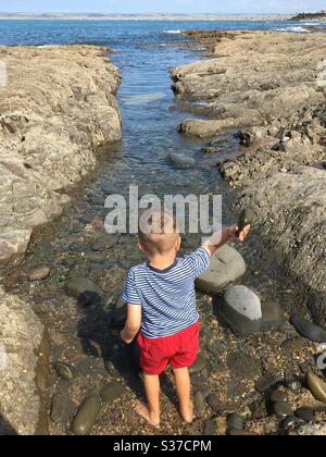 Boy throwing rocks and stones into the sea at Westward Ho!, North Devon Stock Photo