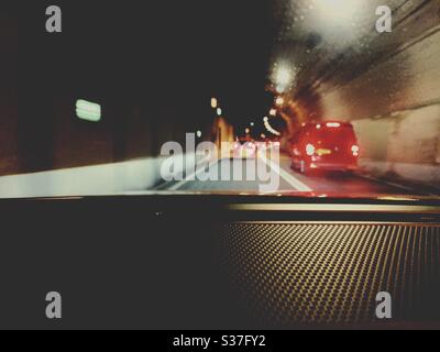 Cars driving through the Tyne Tunnel in North East England. Blurry red brake lights are seen through the windshield. Transport infrastructure. Stock Photo